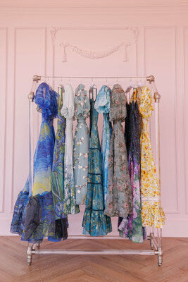 JessaKae Artist Collection — nine dresses inspired by Van Gogh, Monet, and Renoir, displayed together on a clothing rack