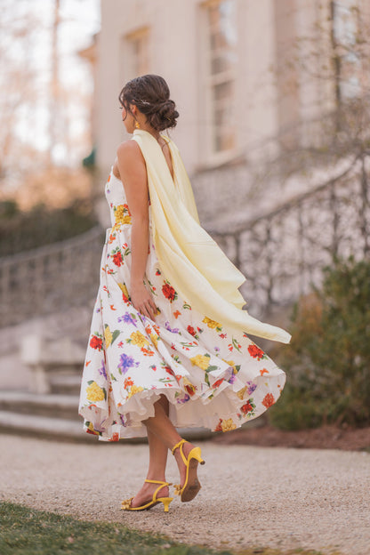 The image shows a woman in a white dress walking down a street, with a building in the background and a few plants on the right side.