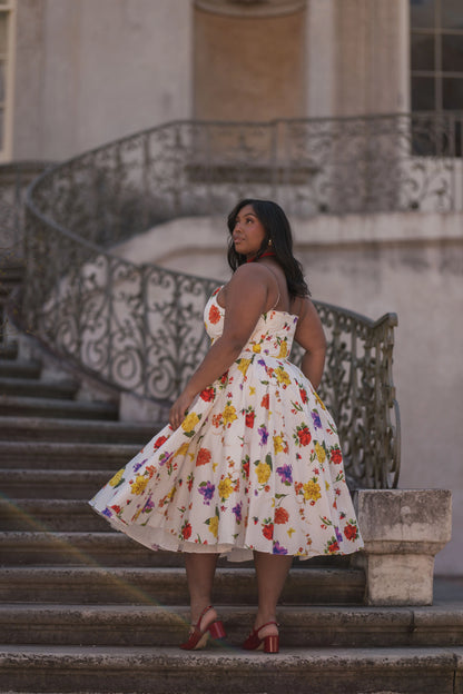 The image shows a woman in a white dress standing on the steps of a building, with a railing and a wall in the background. She is wearing a fashionable dress, likely from the latest fashion trends of