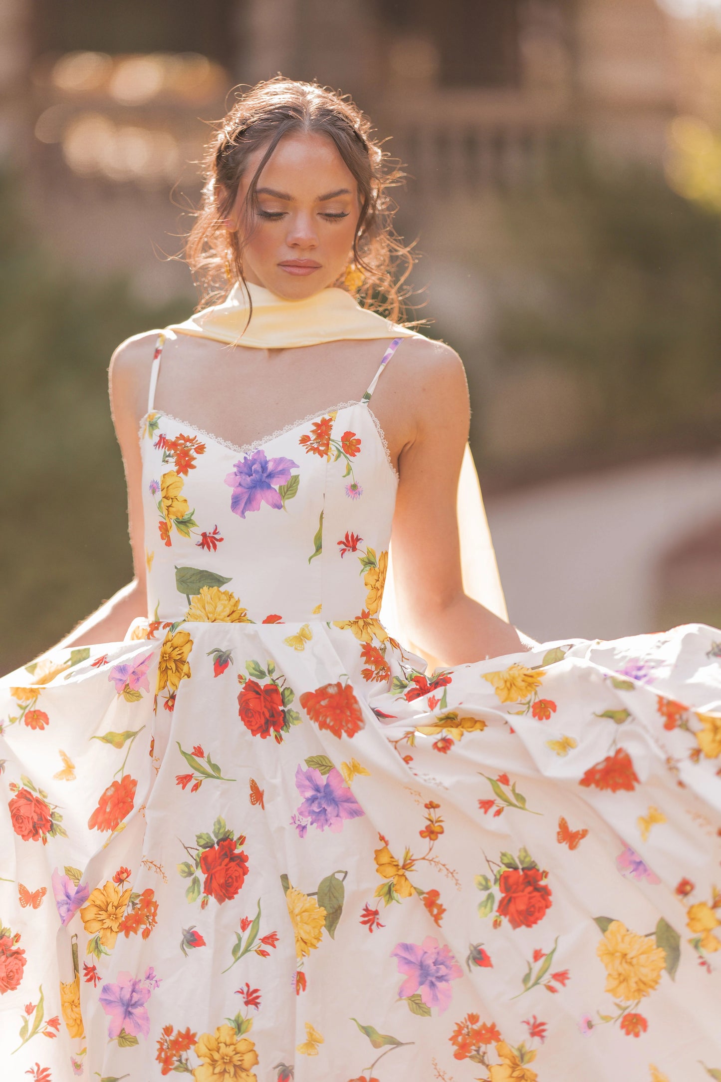 The image shows a woman in a white dress with a floral pattern, standing in front of a blurred background. She is wearing a dress from the 2015 Spring/Summer collection, which is available for