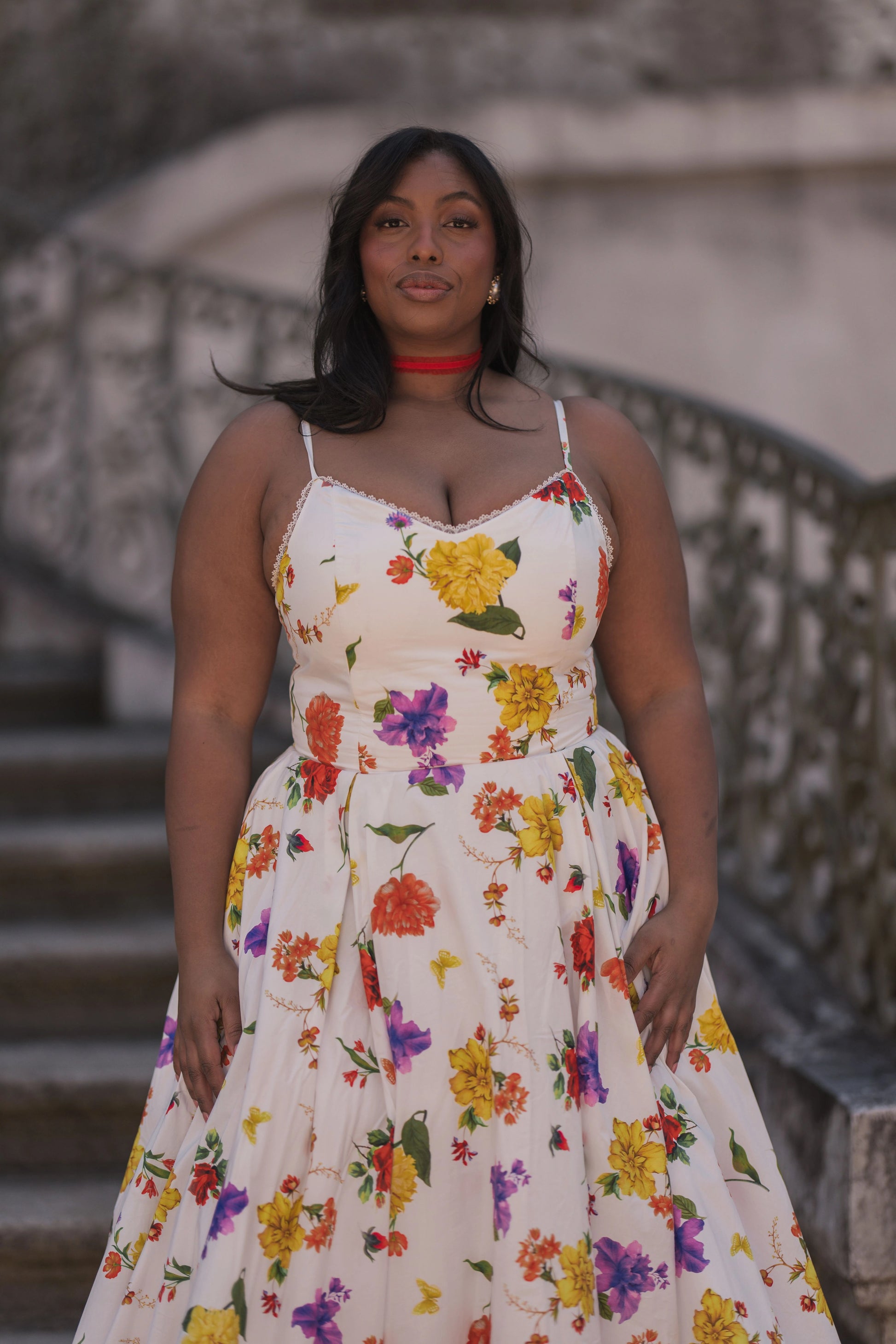 The image shows a woman in a white dress standing on a set of stairs, with a blurred background. She has a human face and is wearing a dress with a pattern of flowers.
