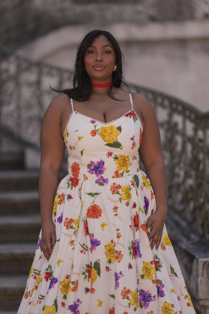 The image shows a woman in a white dress standing on a set of stairs, with a blurred background. She has a human face and is wearing a dress with a pattern of flowers.