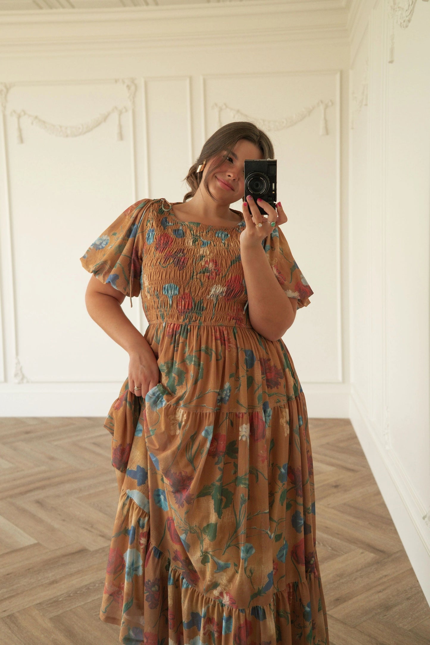 The image shows a woman taking a selfie in front of a mirror, wearing a beautiful dress from the 2015 Spring/Summer collection. She is standing on the floor, holding a camera in her hands, with a